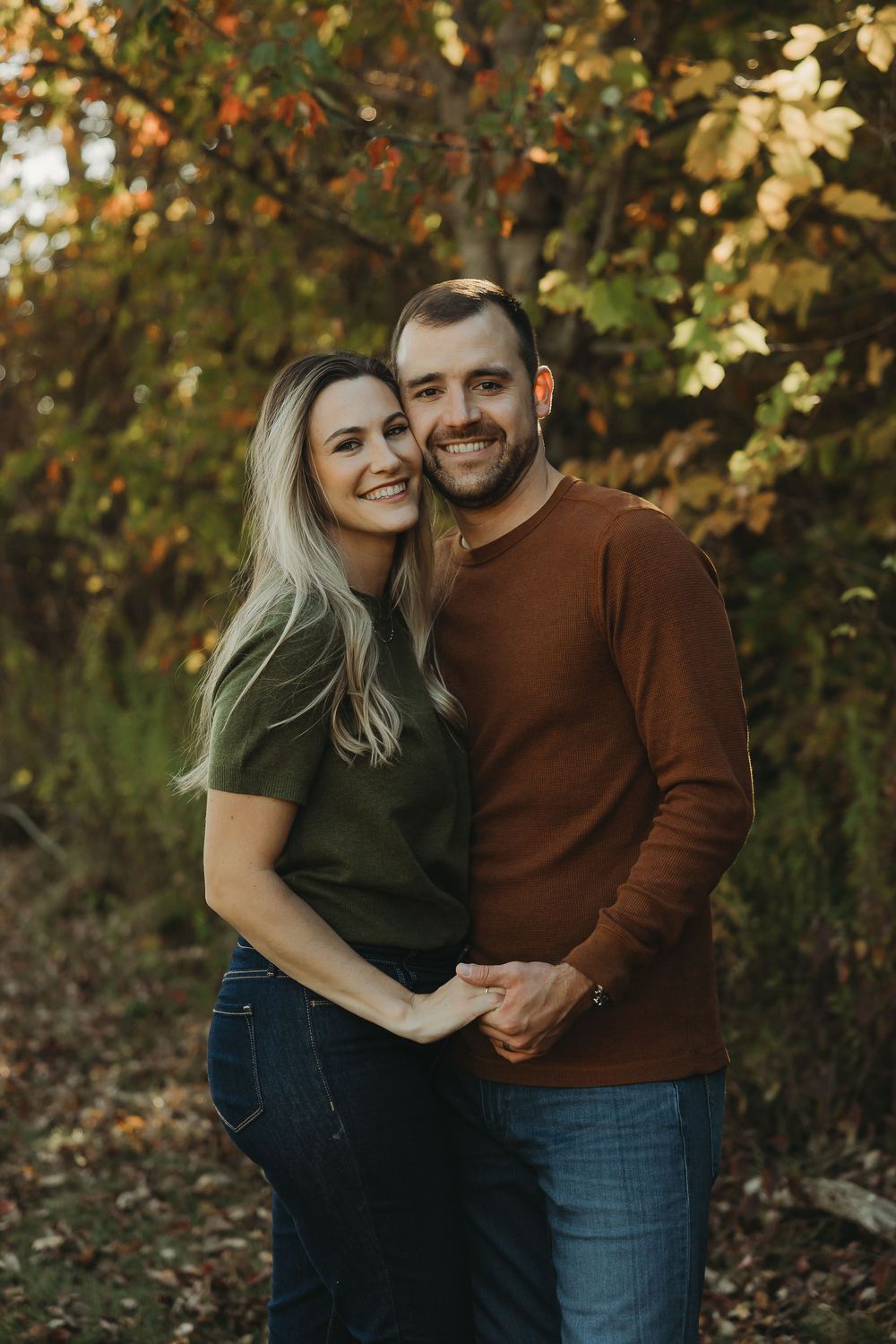 A couple shares intimate moments in a fall setting with autumn foliage in the background.
