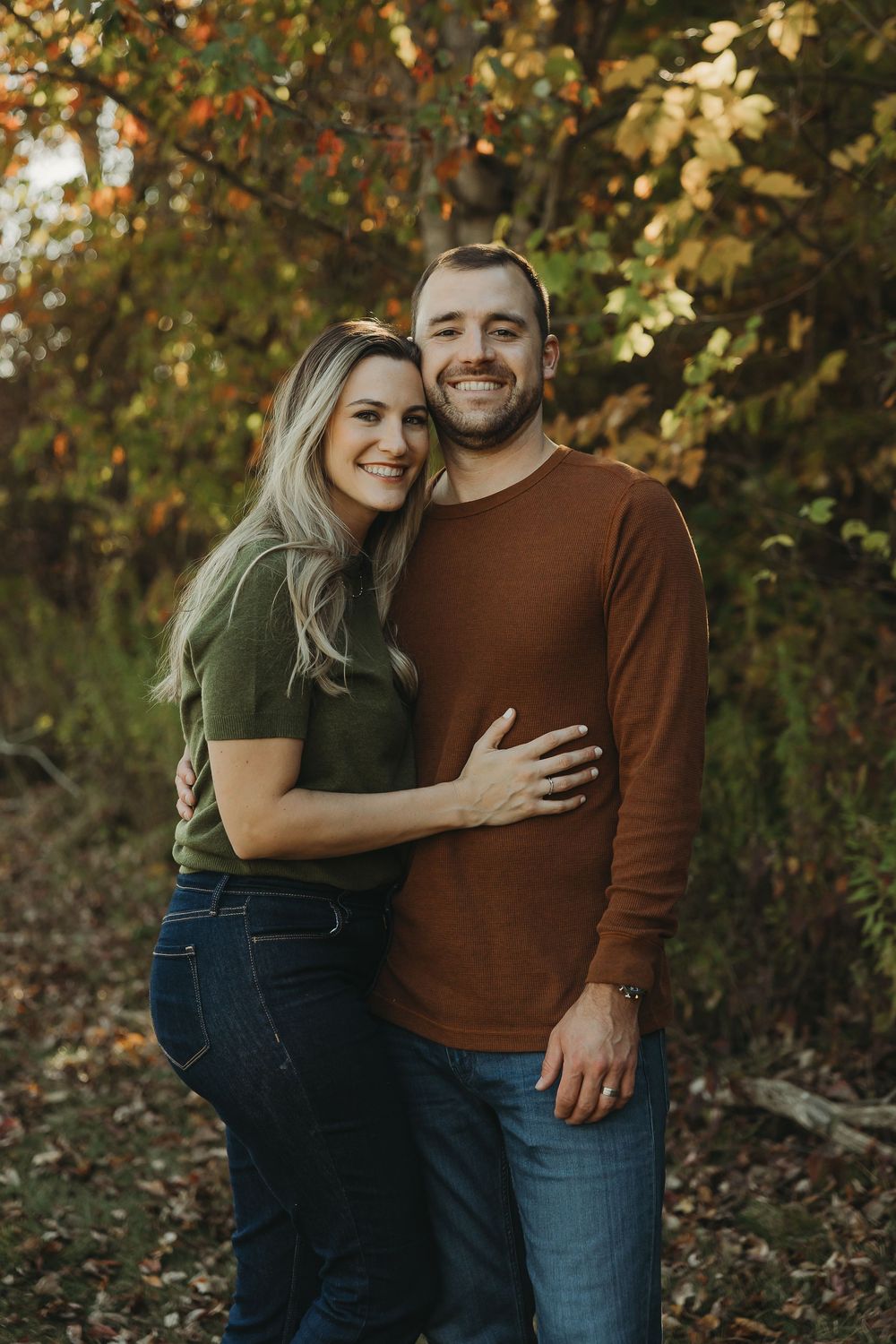 A couple embraces outdoors during autumn with golden leaves in the background.