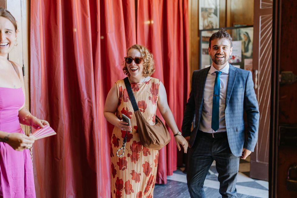 A couple in formal attire shares a joyful moment in front of red curtains during a wedding celebration.