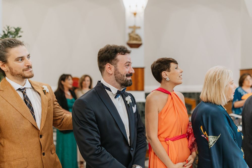 Wedding guests seated in church pews during an indoor ceremony with warm lighting.