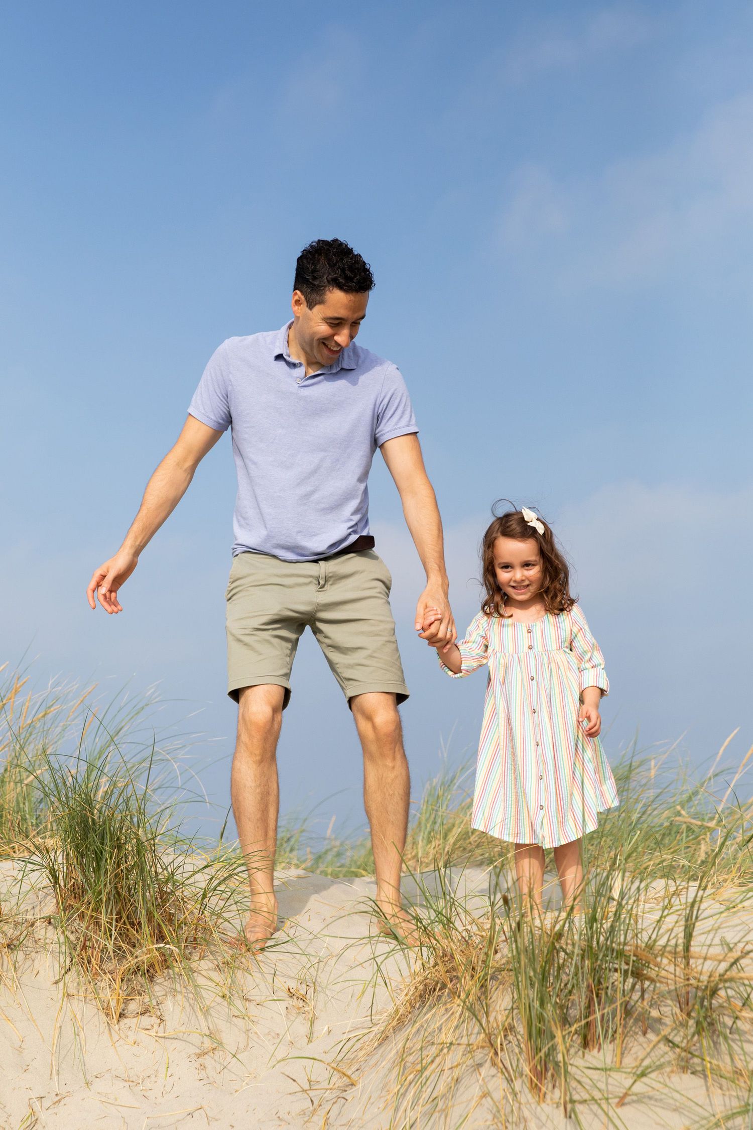 Two people walking together through sand dunes on a sunny beach day.