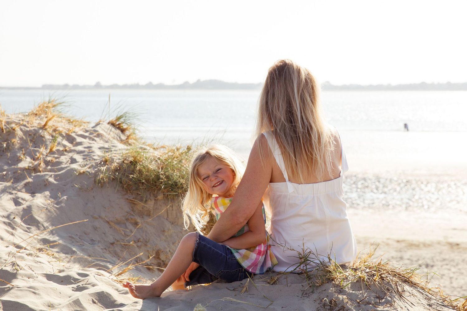 Two people sitting together on sandy beach dunes at sunset.