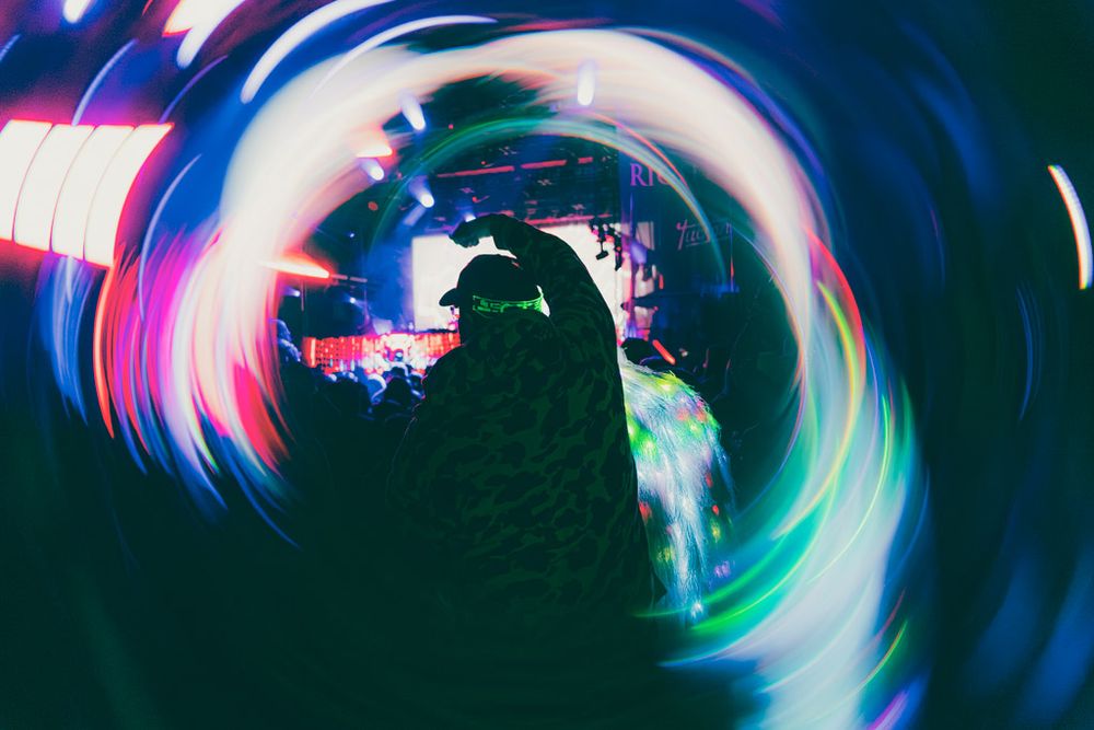 Abstract light trails create a swirling neon vortex pattern against a dark background.