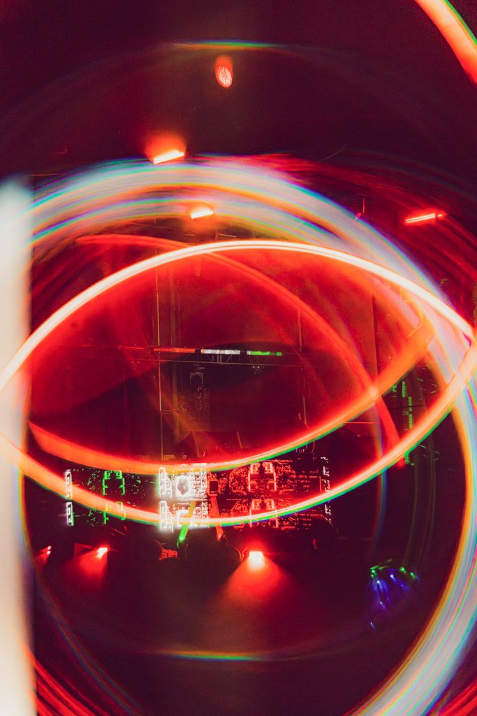 Long exposure light painting creates glowing red and white curved streaks against a dark background at night.