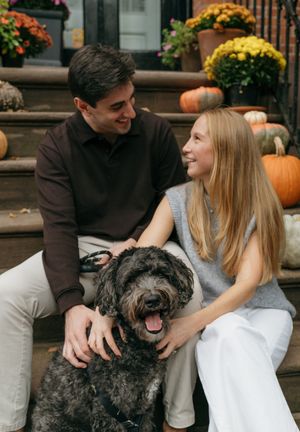 Couple sitting on porch steps with their happy black dog surrounded by fall decorations.