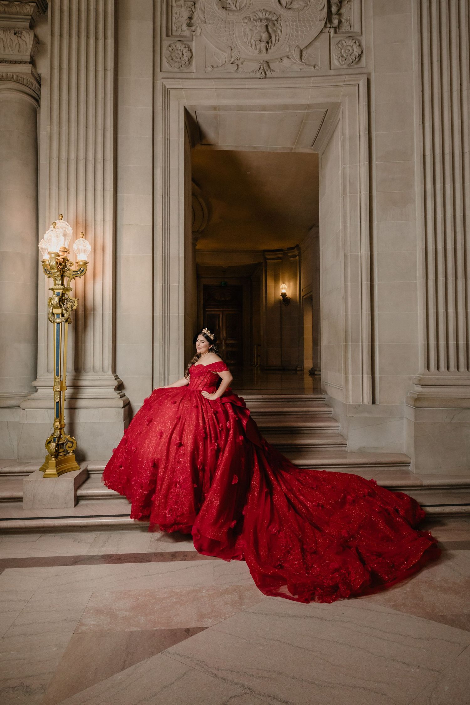 A flowing red formal dress creates a dramatic silhouette against the marble floors of an elegant building.
