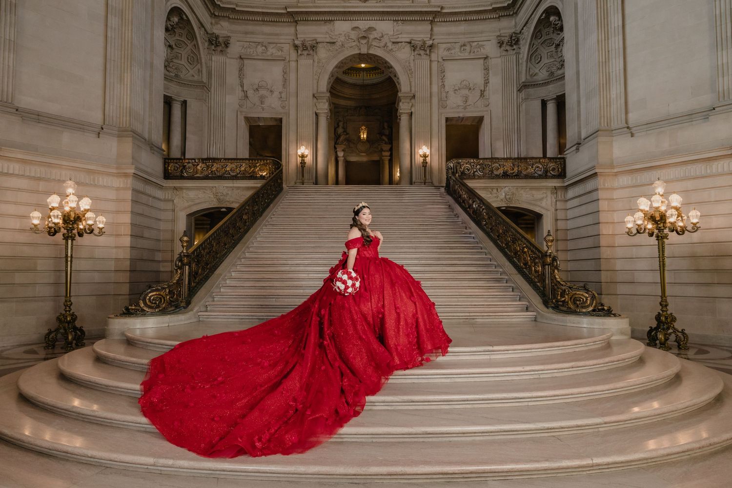 A stunning red ball gown with a dramatic train flows across an ornate marble staircase in a grand palace interior.