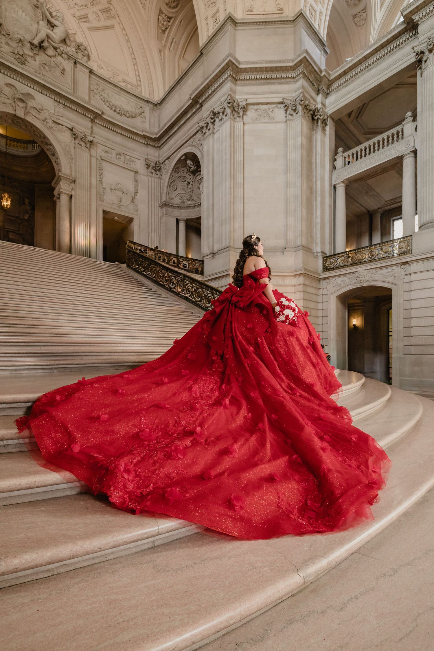 A stunning red ballgown with a voluminous skirt cascades down marble stairs in an elegant classical building.
