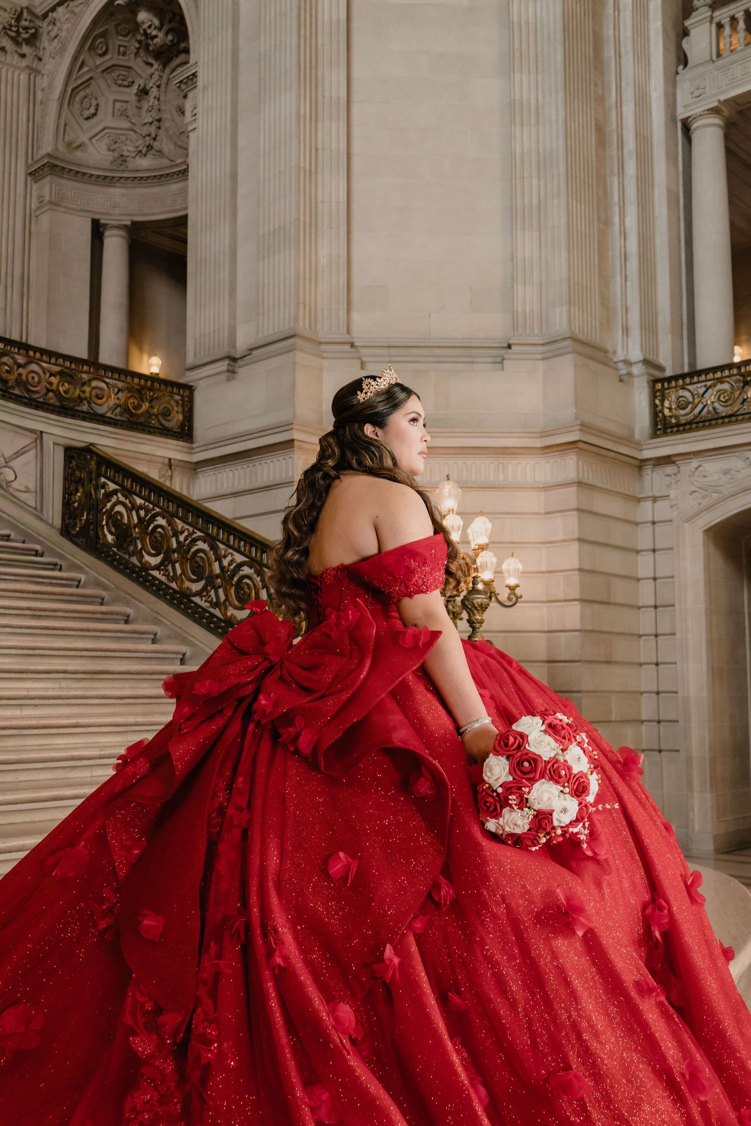 A stunning red ballgown photographed in a grand marble hallway with ornate architectural details.