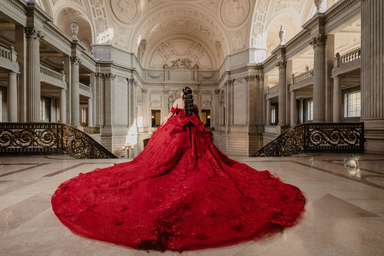 Multiple views of a flowing red ballgown with dramatic train displayed in a historic building's marble corridor.
