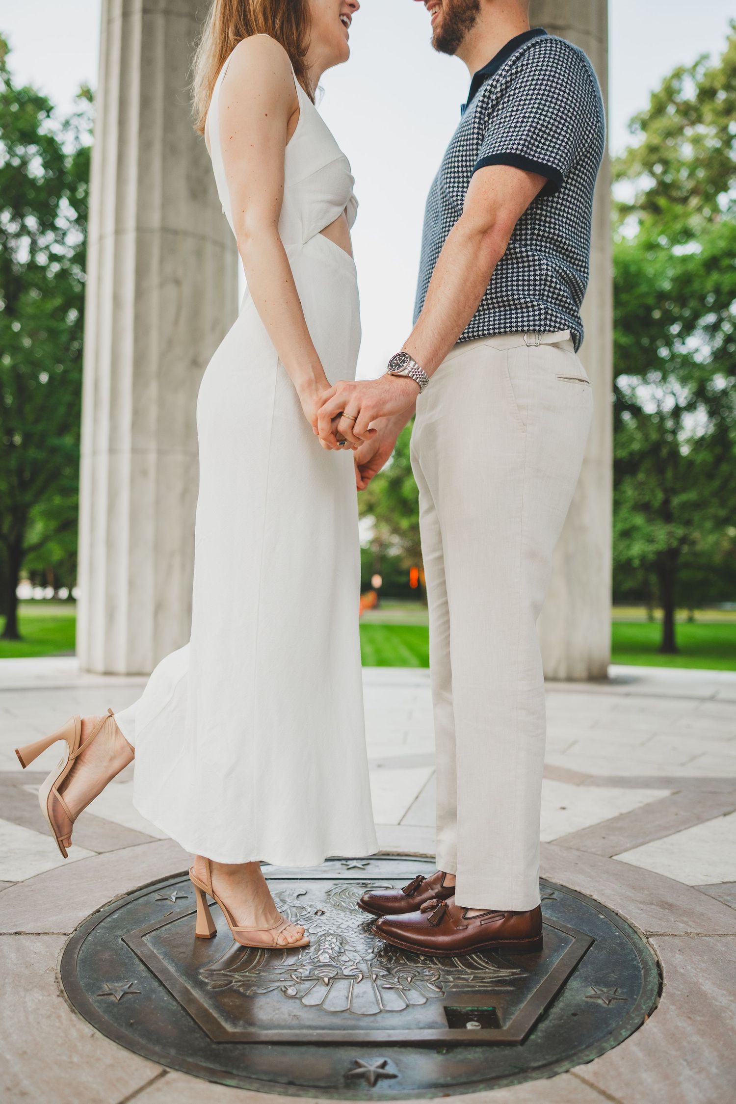 A couple stands on a manhole cover wearing contrasting formal shoes - one in sneakers and one in dress shoes.