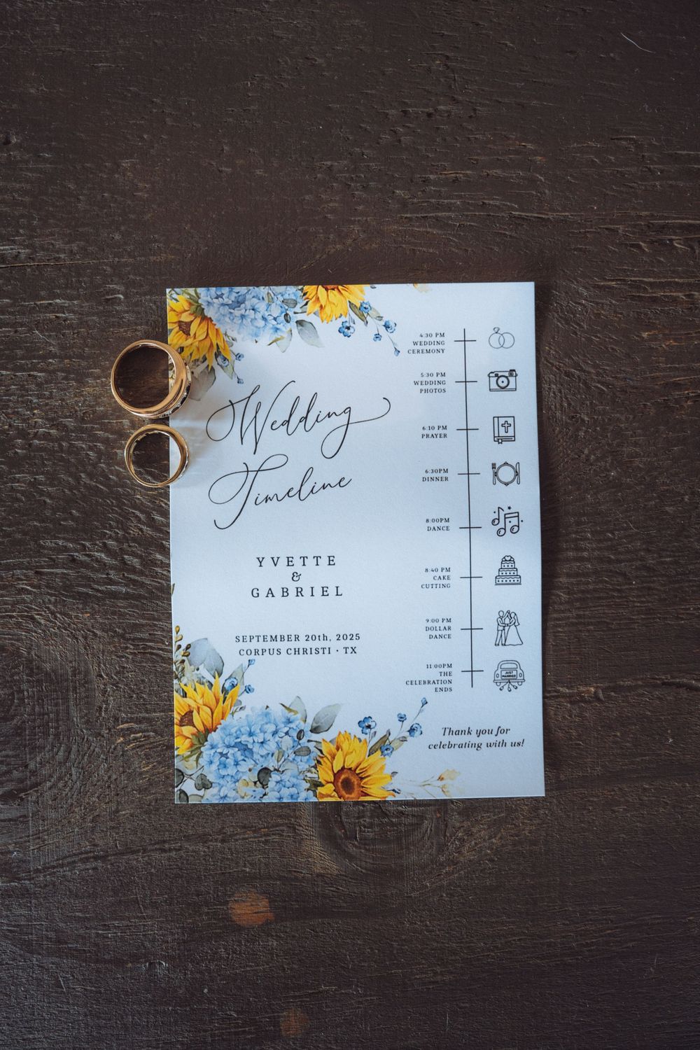Wedding invitation with blue floral design and sunflowers on dark wooden background.
