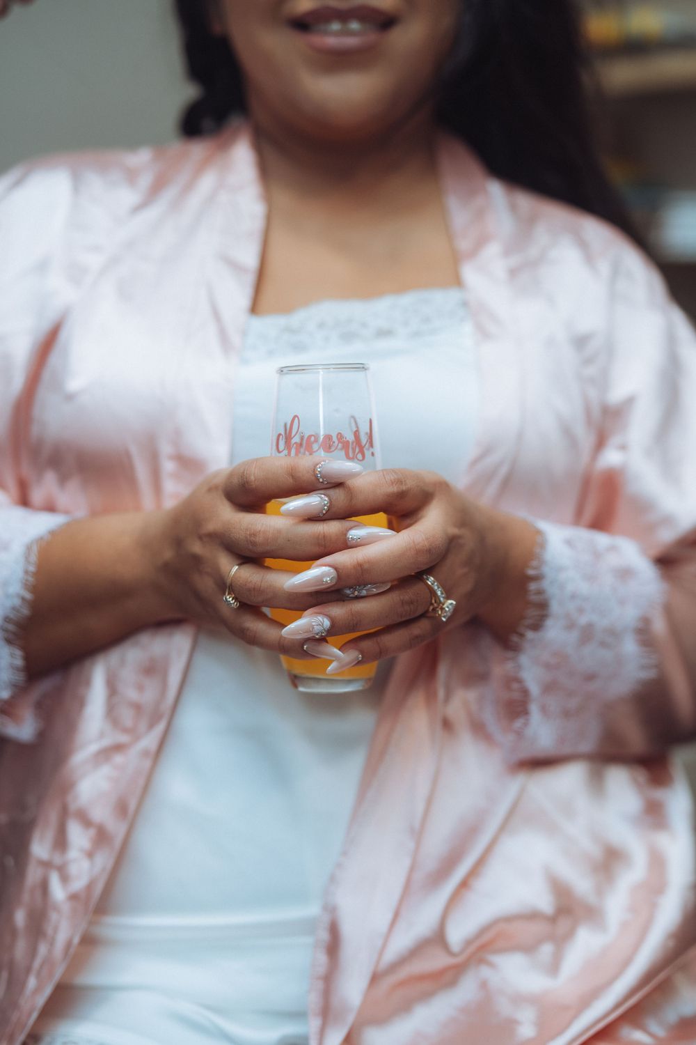 Close-up of hands holding drink in pink satin robe during wedding preparations.