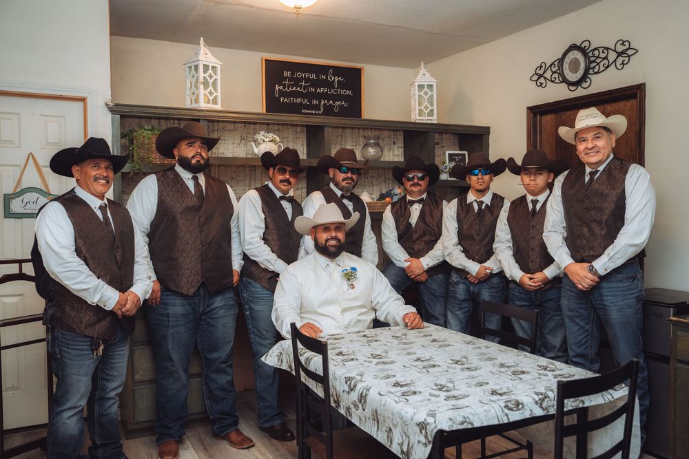 Group of groomsmen in western attire lined up against a wall.