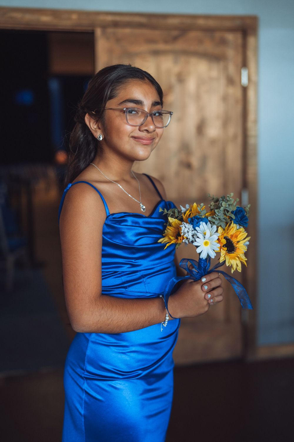 Bridesmaid in royal blue satin dress holding sunflower bouquet.