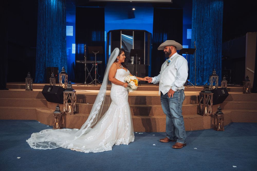 A couple shares a romantic moment on stage with the bride in a lace wedding gown and groom in western attire.