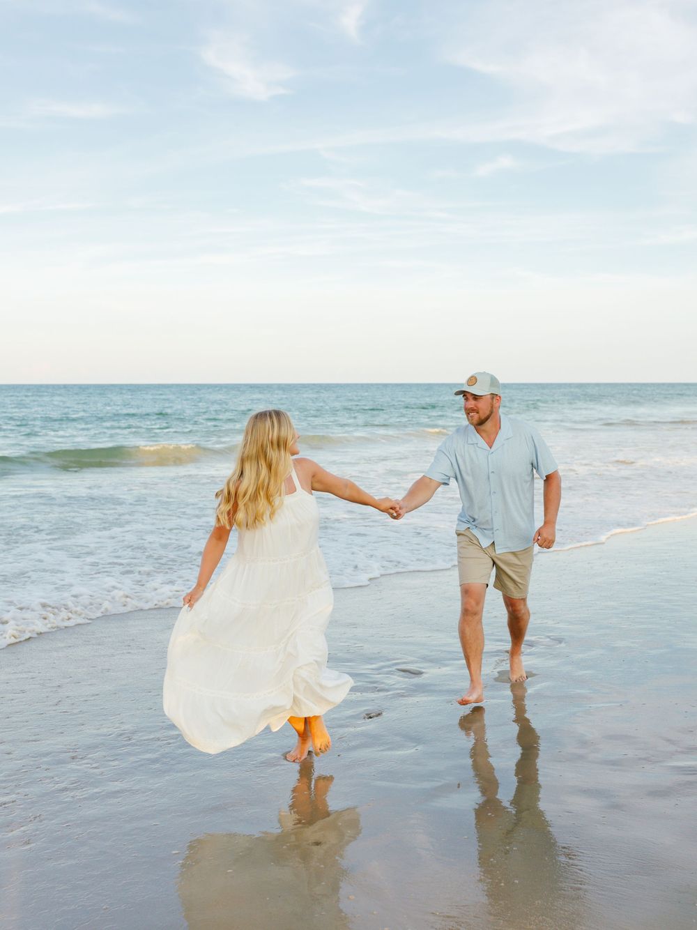Couple holding hands while walking along ocean shoreline at sunset.