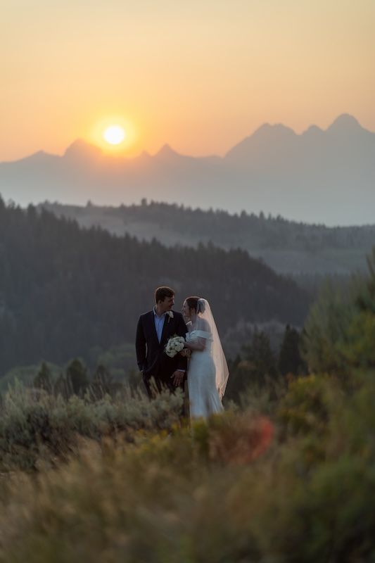 Bride and groom share a romantic moment at sunset with Grand Teton mountains in the background.