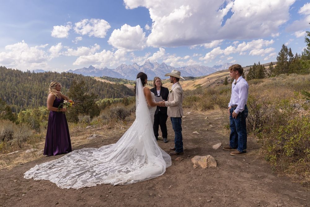 A scenic mountain wedding photoshoot with a dramatic cathedral-length lace train flowing across rocky terrain.