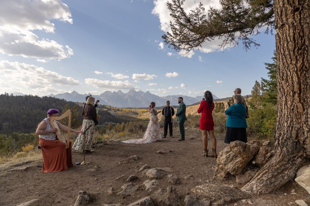 People gather on a mountain overlook with scenic views of distant peaks and valleys.