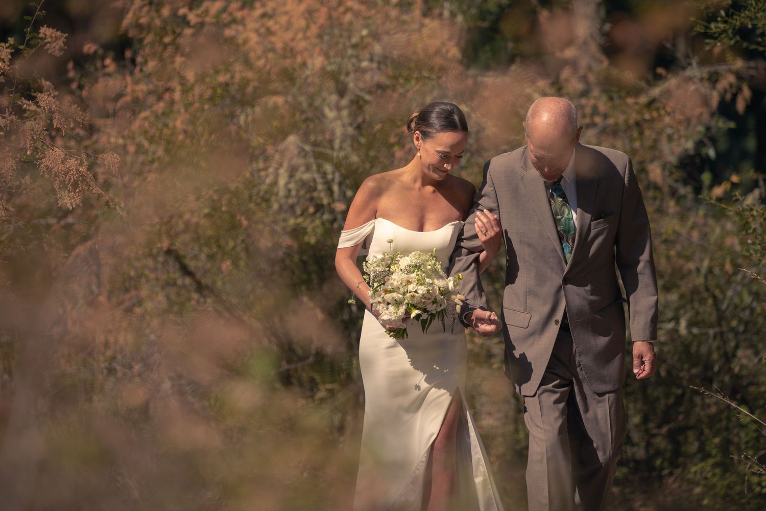 Wedding party walking through autumn foliage during outdoor celebration.