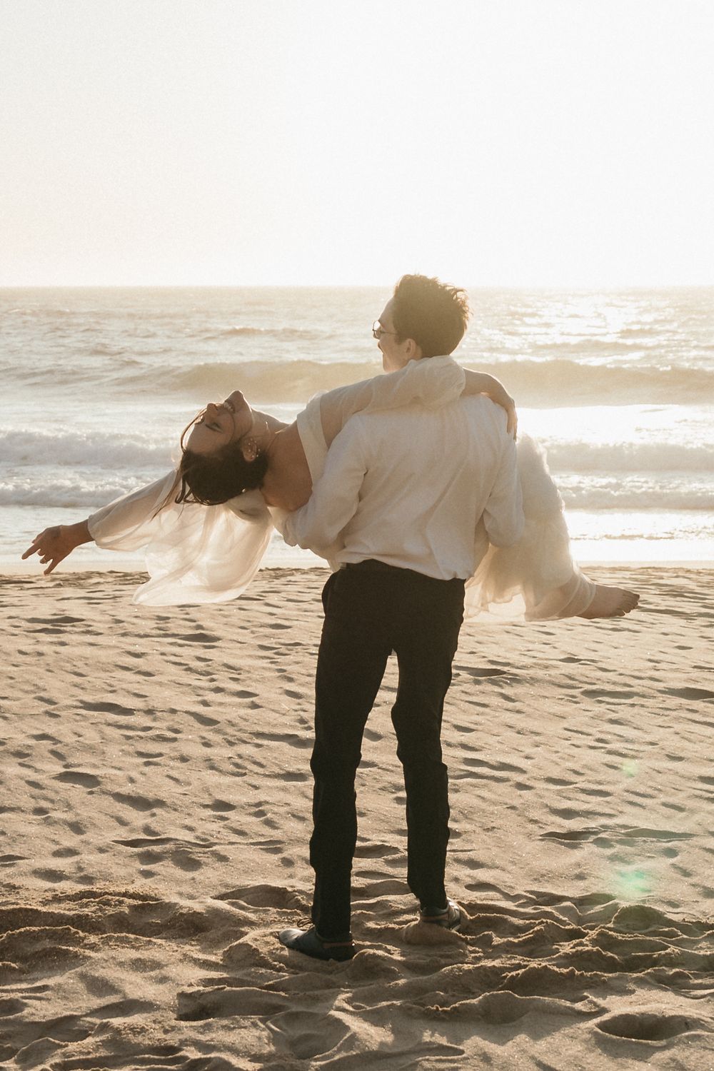 A playful dip pose between a couple on a sandy beach at golden hour.