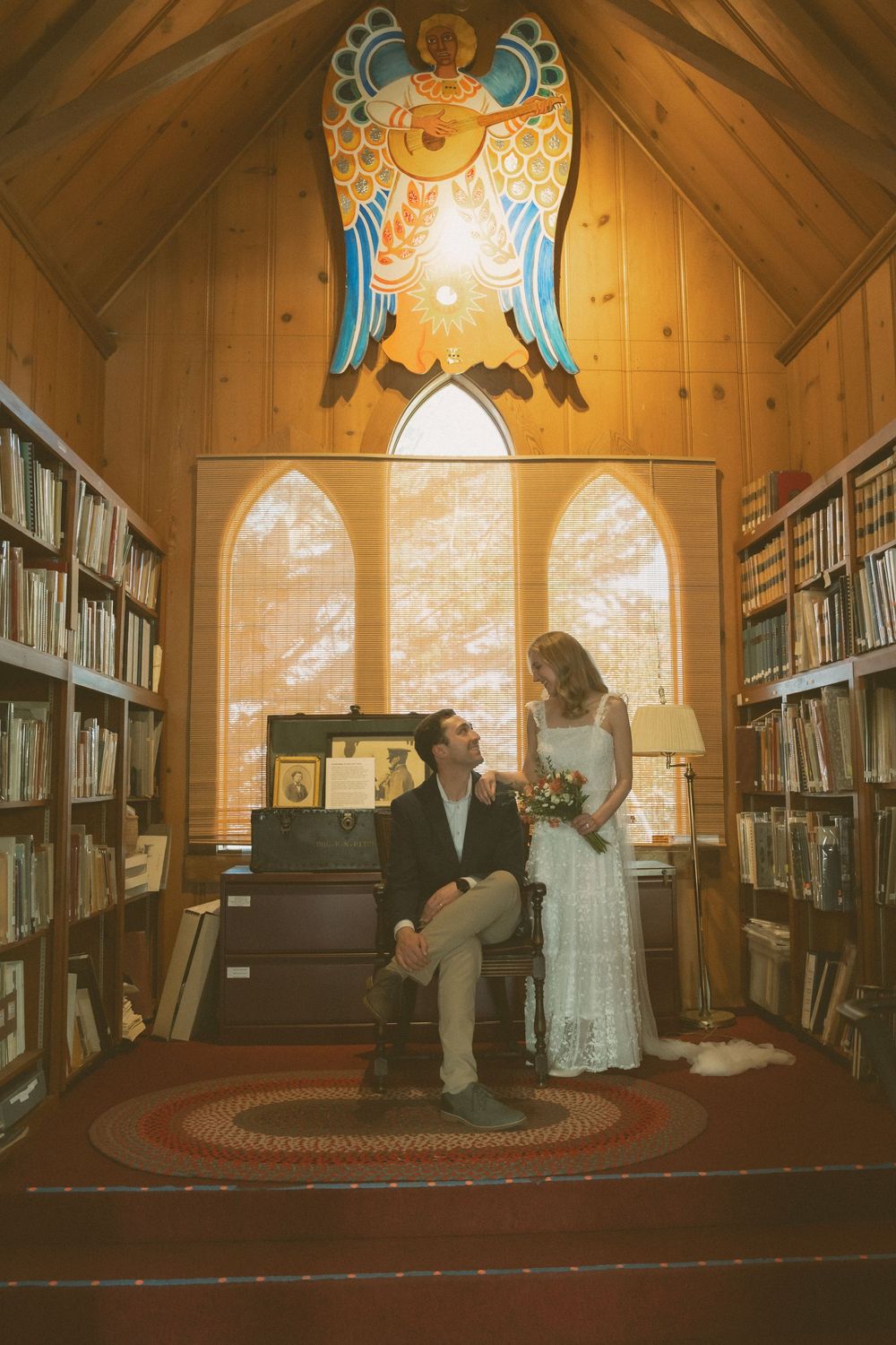 Bride and groom sharing a romantic moment in a cozy wooden chapel library with stained glass.