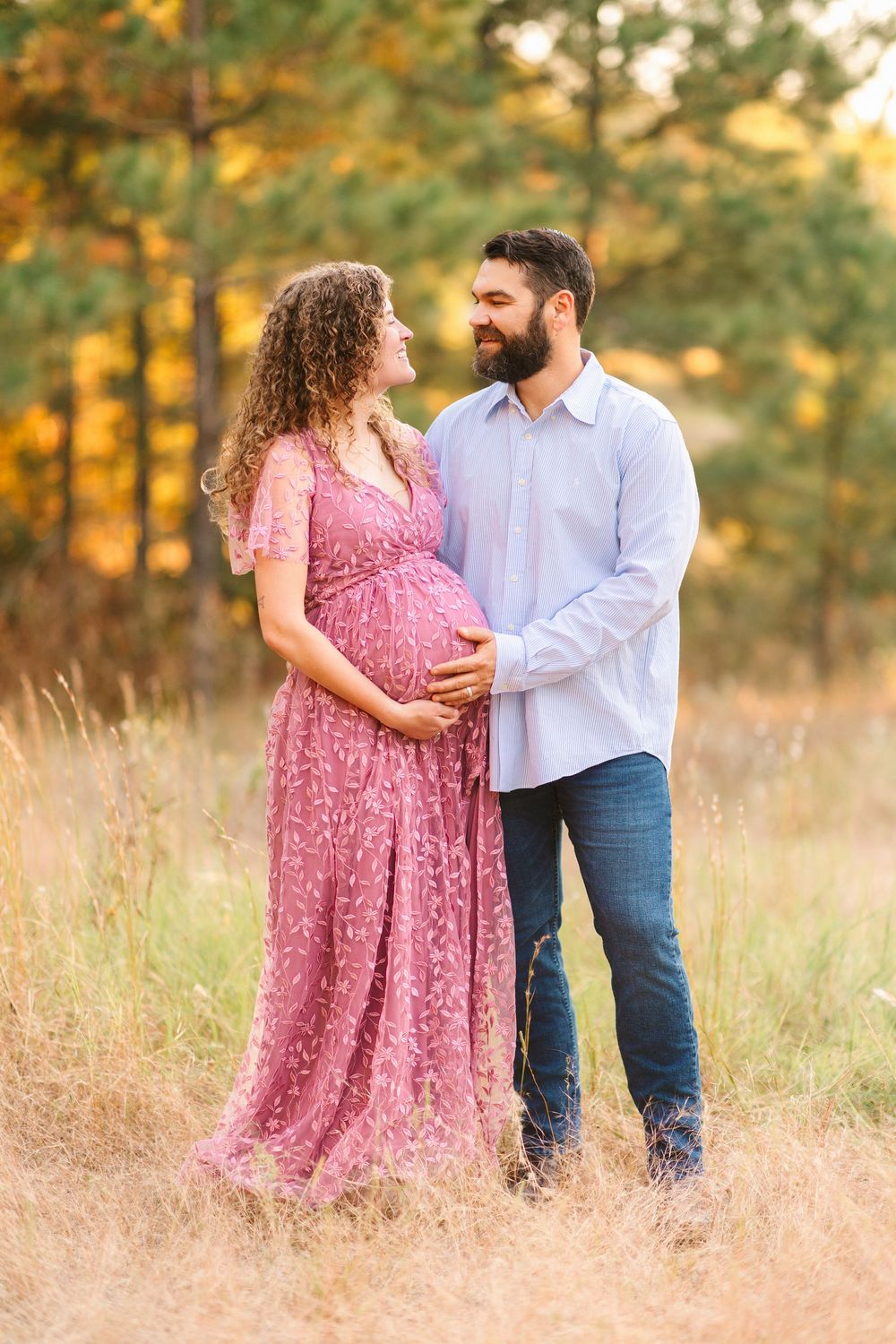 Expectant couple shares tender moments in autumn field during golden hour maternity photoshoot.