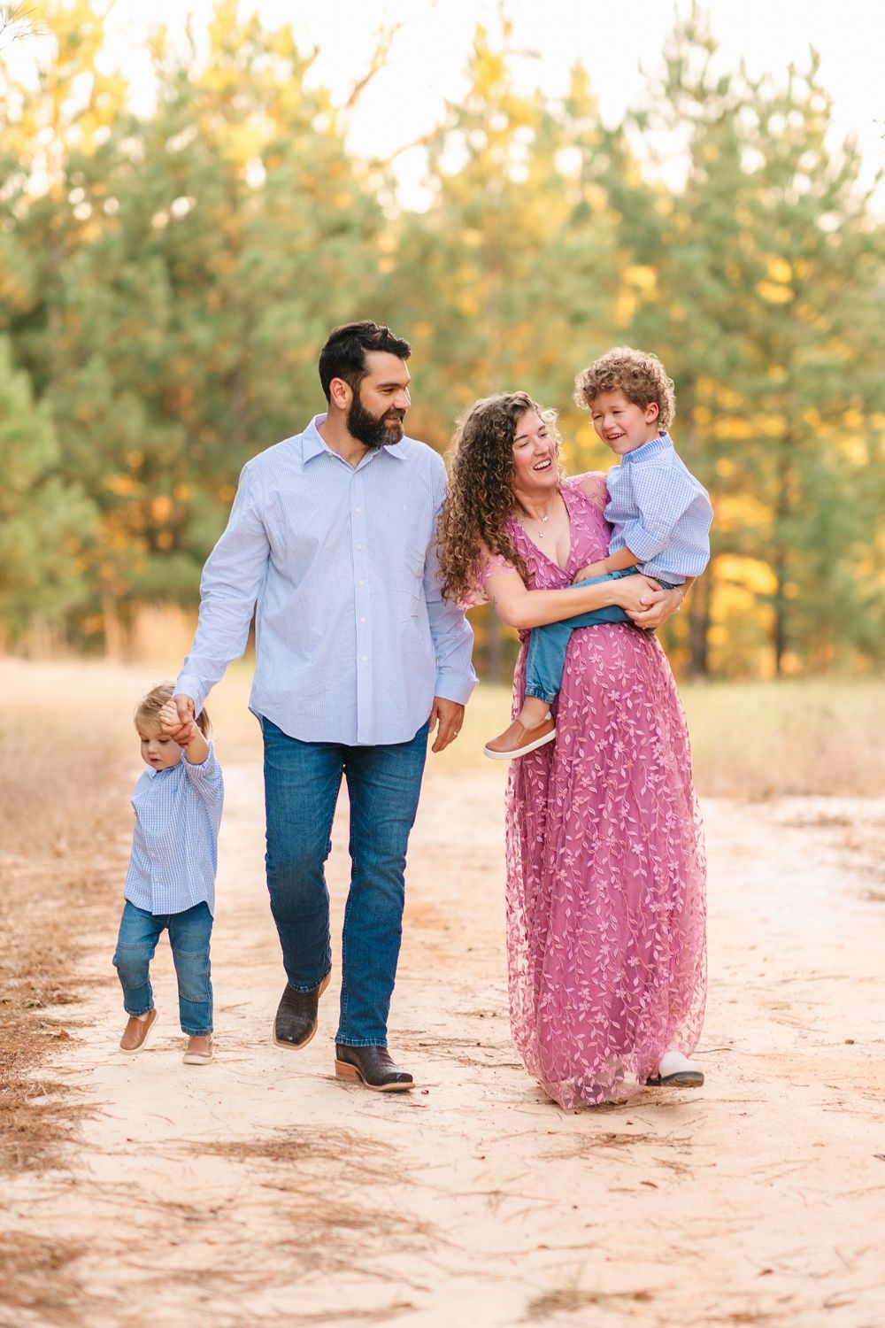 Family of three enjoy playful moments together on sandy ground during sunset photo session.