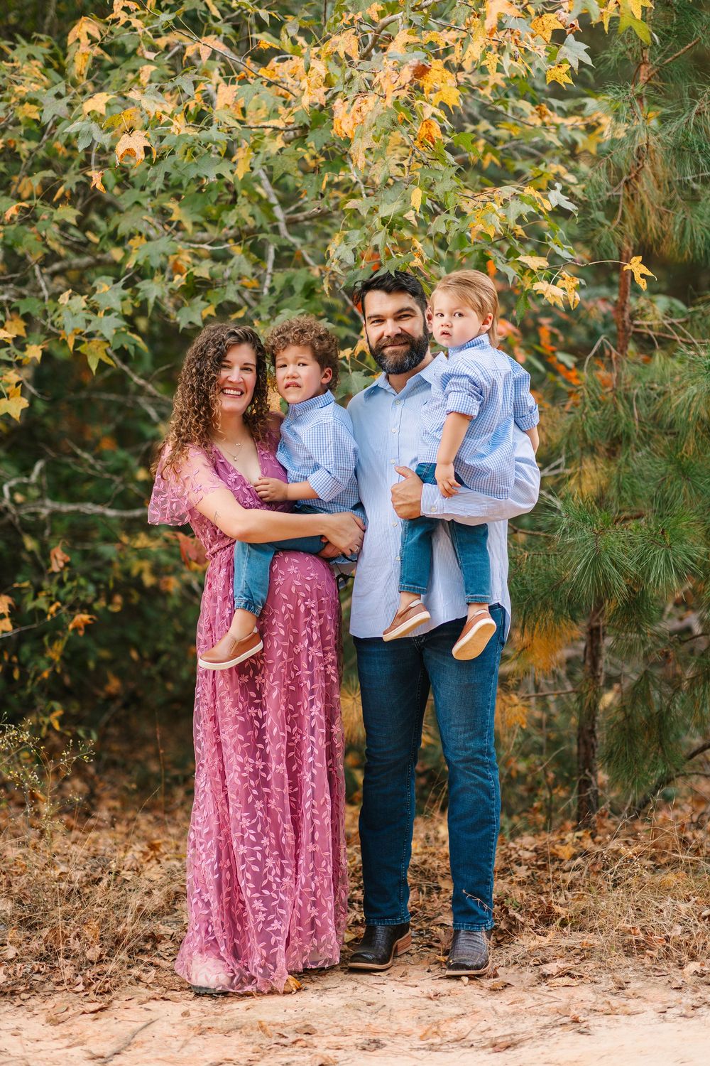 A family shares joyful moments together outdoors among autumn trees and fallen leaves.