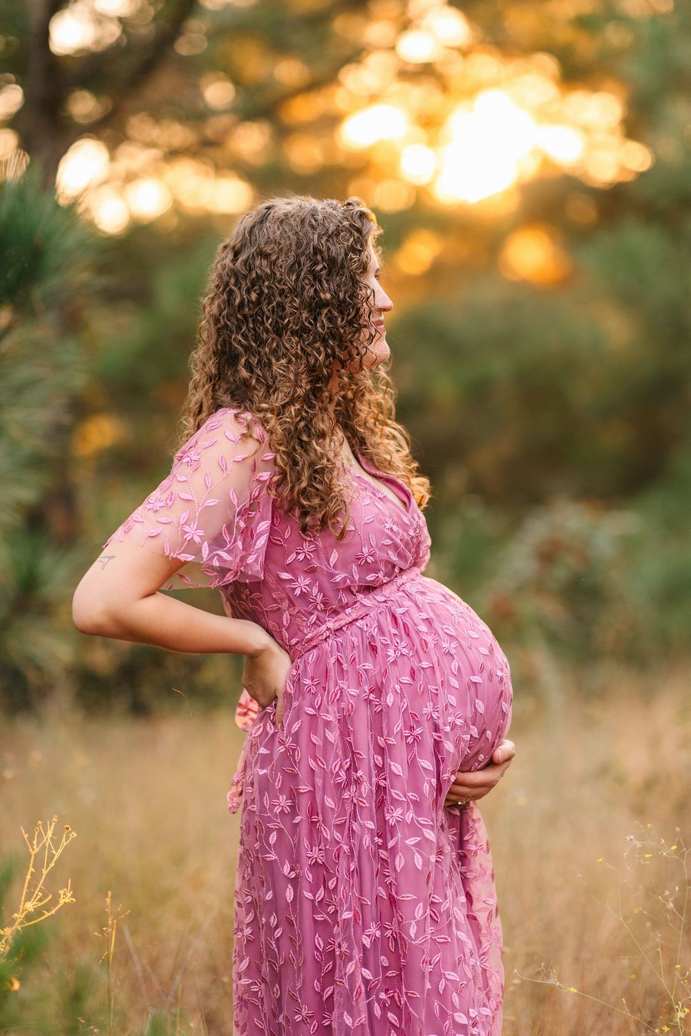 Someone wearing a textured pink dress stands in tall grass during golden hour.