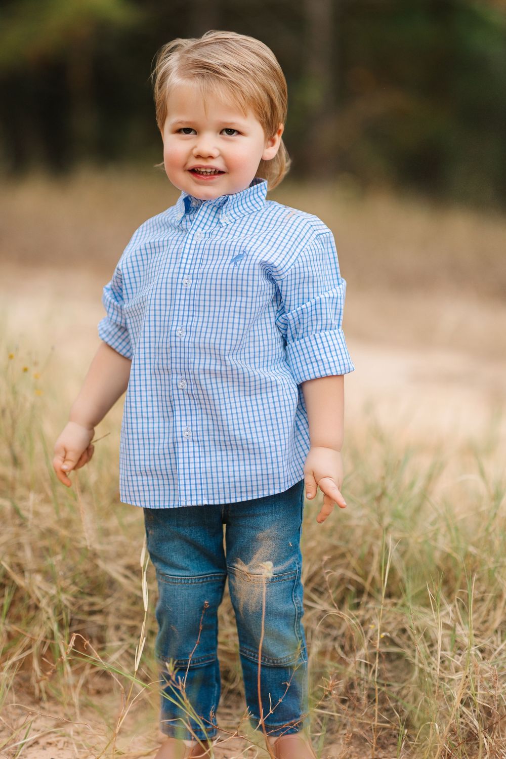Young child walking and playing in a field wearing blue gingham shirt and jeans.