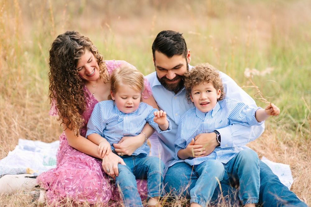 A family enjoying a warm autumn day together outdoors in casual clothing while sitting on brown grass.