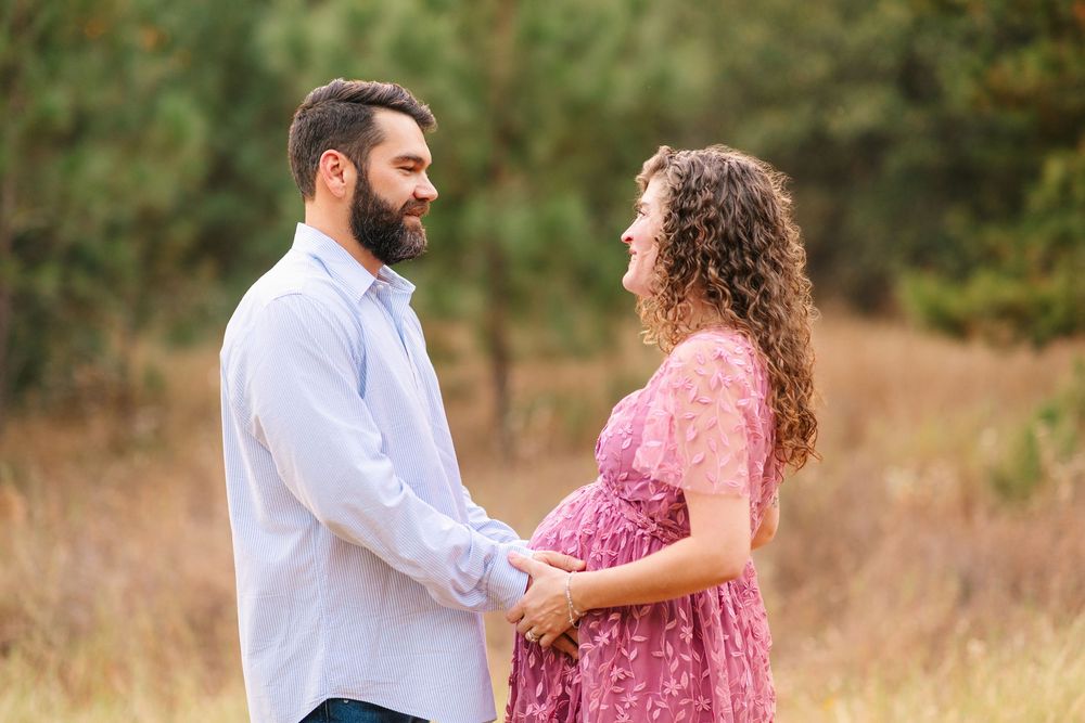 A couple in white and pink clothing laughs together while walking in a sunny outdoor field.