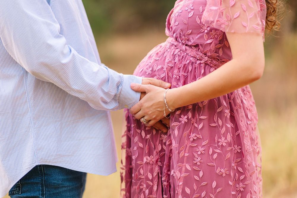 Two people hold hands outdoors, one wearing a pink floral dress and the other in a white shirt.