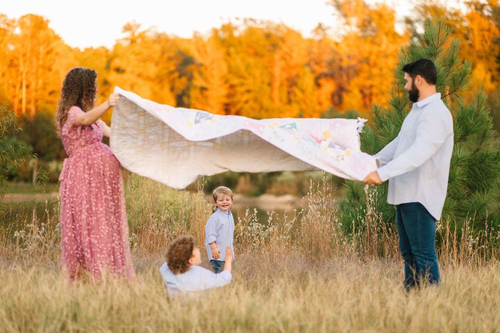 A young family plays together with a white blanket in a golden autumn field during sunset.