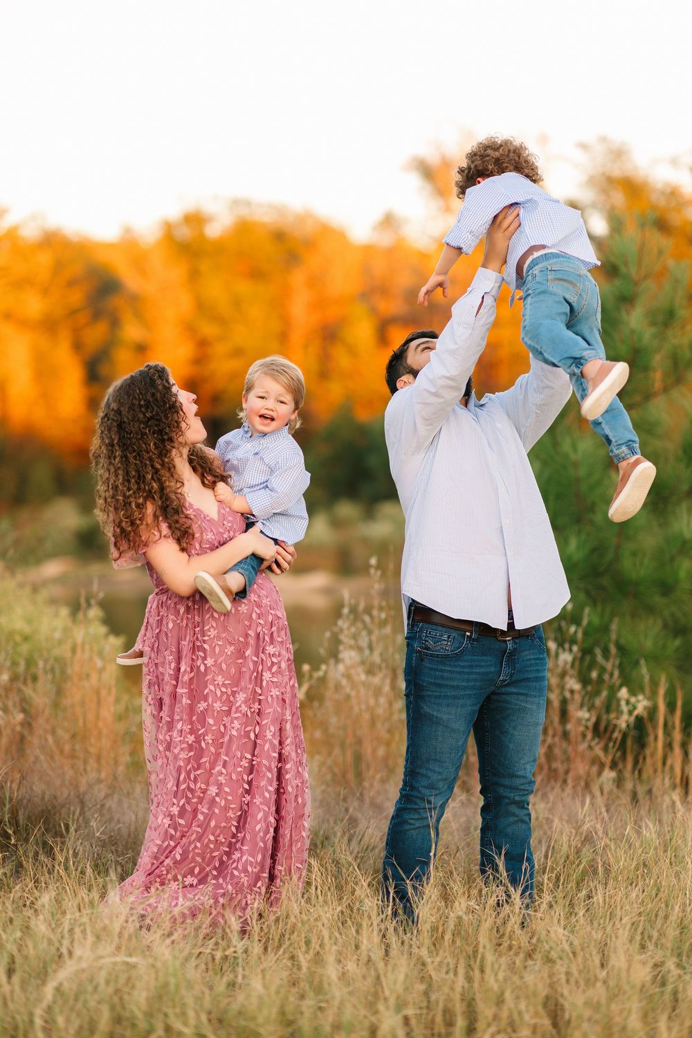 A joyful family plays together in a sun-drenched autumn field with tall golden grasses during sunset.