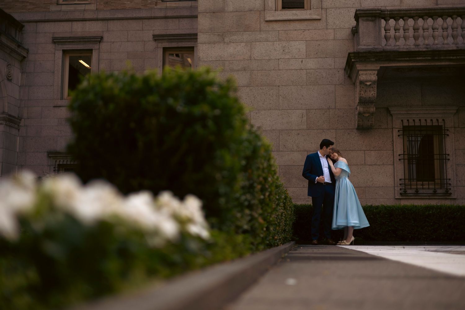 Elegant classic stone building exterior with bride and groom sharing a romantic moment in formal wedding attire.