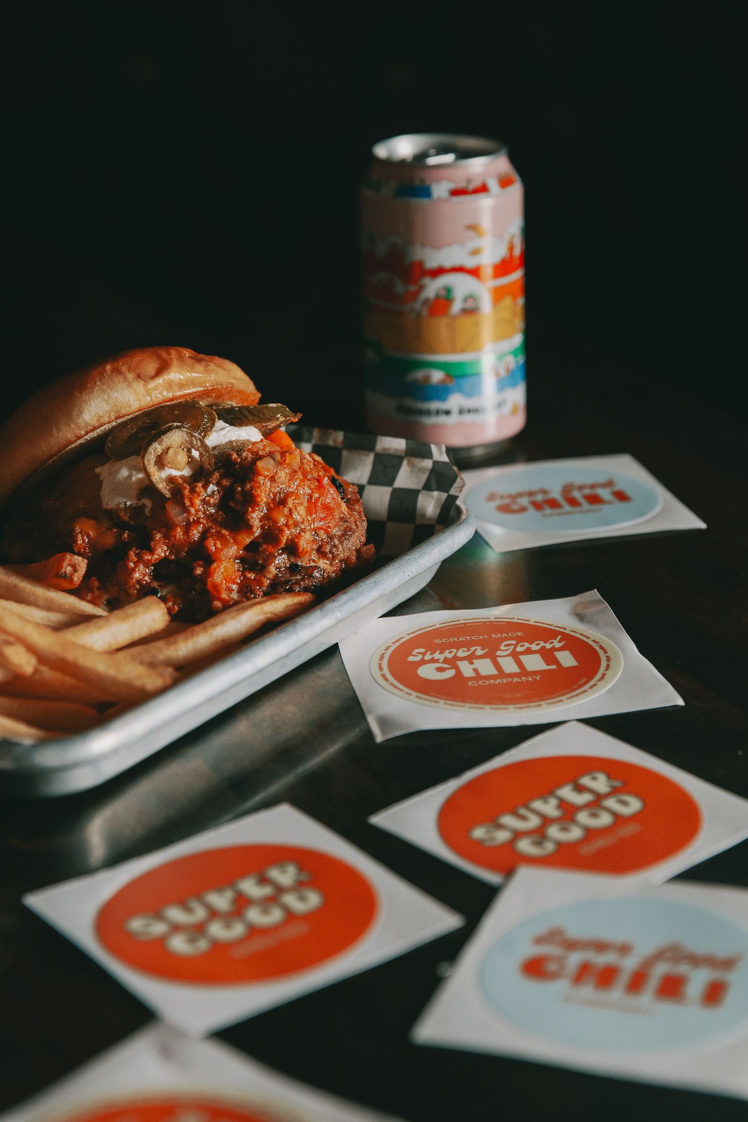 A pulled pork sandwich on a wooden board sits beside a glass of craft beer in moody lighting.