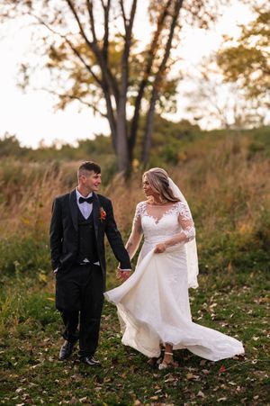A bride and groom share a joyful moment together on fallen autumn leaves in a scenic outdoor setting.