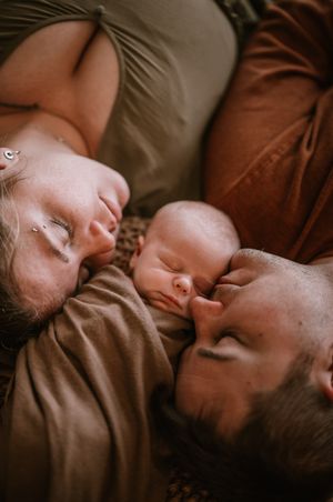 Sweet family moment as they lie together resting quietly on brown blankets in warm lighting.