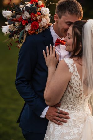 A tender wedding moment captured with a vibrant red and white bouquet and elegant lace dress details.