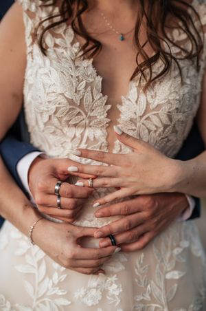 Close-up sequence of hands wearing wedding rings against delicate white lace wedding dress details.