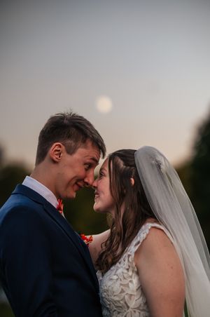 A romantic wedding moment at sunset with a bride in lace dress and groom in navy suit sharing an intimate moment.