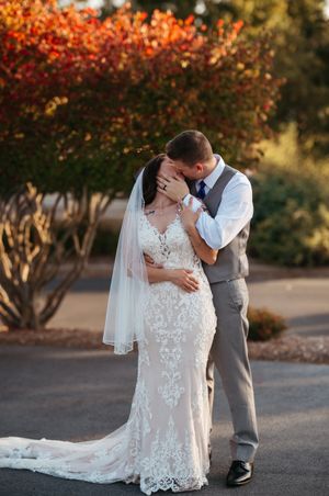 A romantic wedding couple shares an intimate moment under autumn trees with vibrant orange and red foliage.