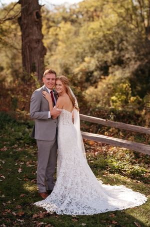 A couple in wedding attire share intimate moments on a wooden bridge surrounded by autumn foliage.