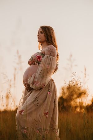A series of silhouetted figures in a floral dress stand against a golden sunset in a grassy field.