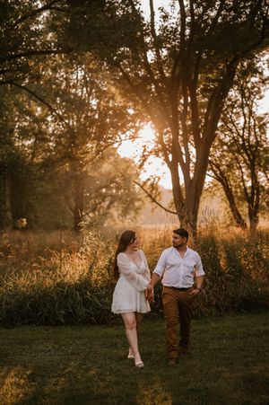 Romantic sunset photoshoot in a wooded field with golden light streaming through trees creating dreamy atmosphere.
