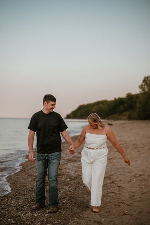 A couple walks along a serene beach at sunset, leaving footprints in the sand.