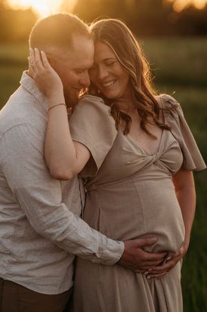 A couple shares an intimate moment at sunset during a maternity photoshoot in a golden-lit outdoor setting.